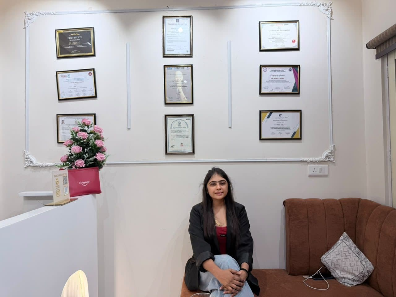 Dr. Nikita Soni seated in front of her wall of framed certificates